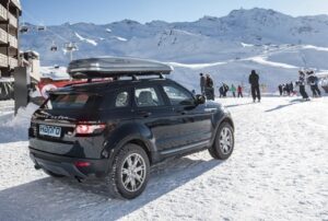 Černé auto na horách s Hapro střešní boxy s pozadím zasněžené krajiny a lyžaři a vlek