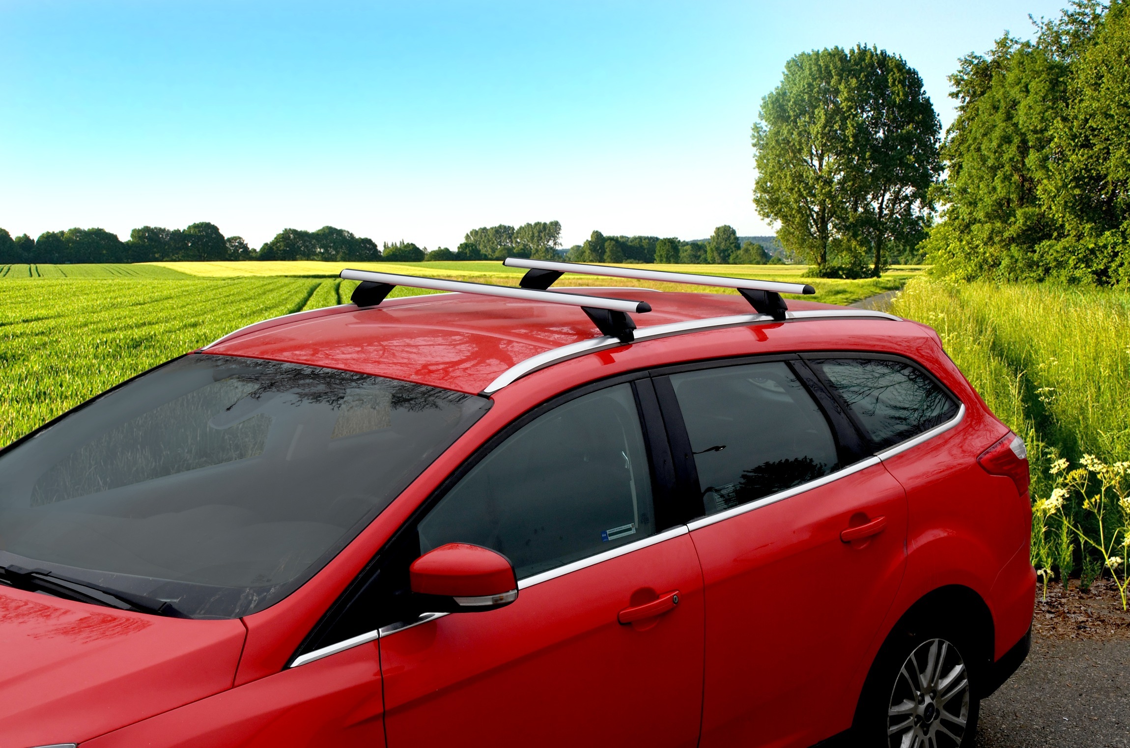 střešní nosiče Compass integrované podelníky na červeném autě v pozadí s polem a stromy