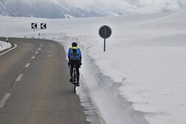 Cyklista na silnici s jízdním kolem zezadu z nosiče kol v zasněžené krajině a dopravními značkami napravo