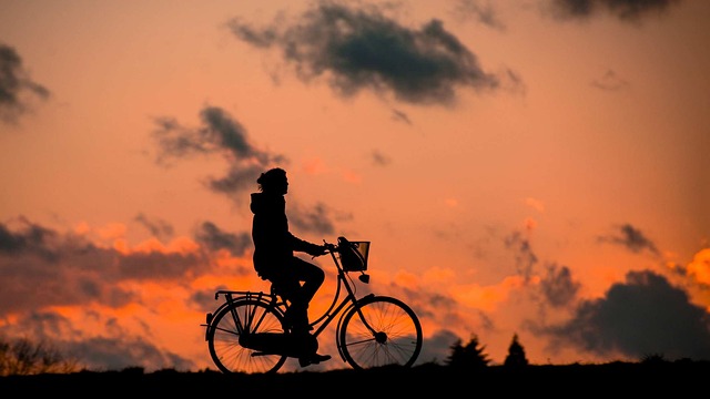 Silueta na kole s košíkem vepředu v pozadí oranžové nebe při západu slunce s mraky