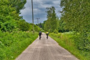 Dva cyklisti na asfaltové silnici obklopení zelení